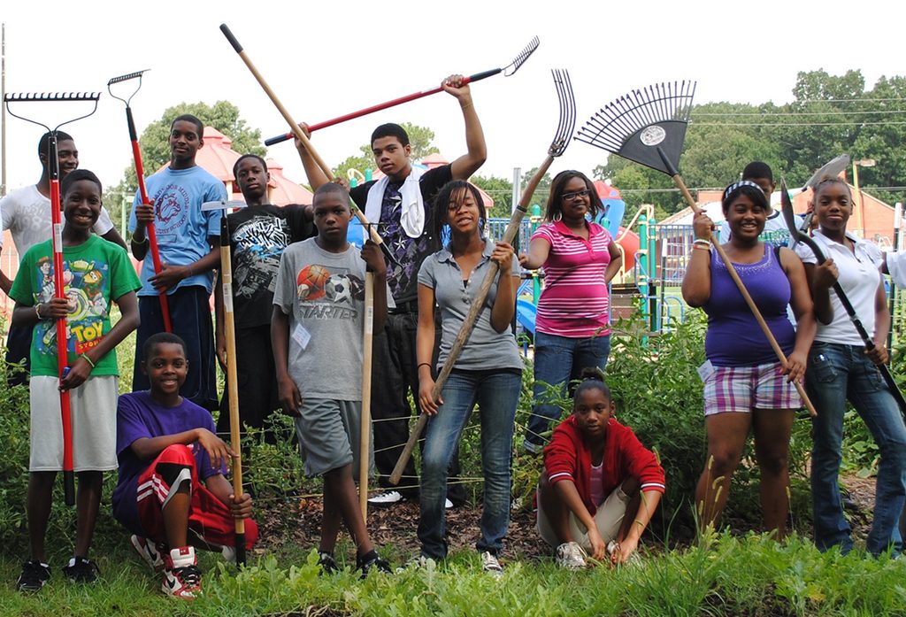 Young people holding rakes and garden tools in a community garden